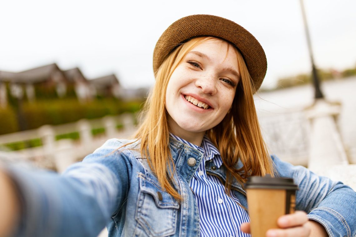 selective focus photo of woman in blue denim jacket holding coffee cup while smiling